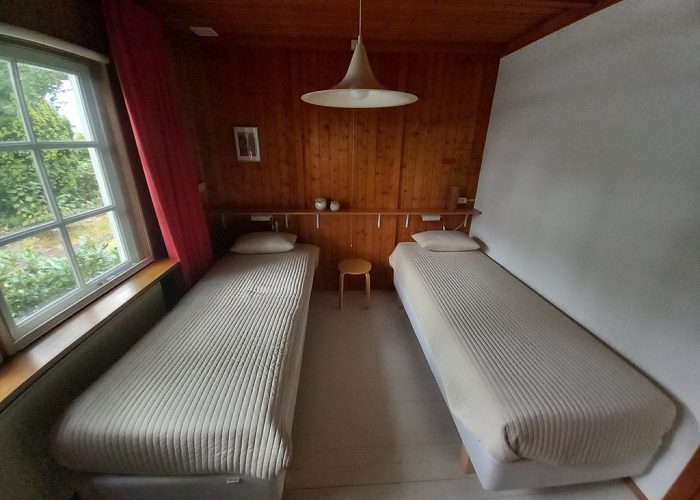 Slaapkamer met twee eenpersoonsbedden in het boshuis, simpel maar functioneel, met uitzicht op de natuur.